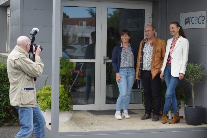 Frédéric Gluzicki prenant une photo d'Alice Ladet, Anne Cordel et de Guillaume Cordel en face de notre logo à l'entrée de l'entreprise